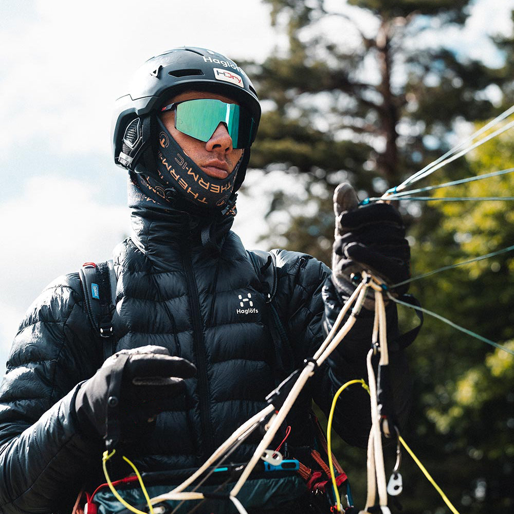 Outdoor-Ski-Ausrüstung Person mit Helm, Skibrille, Daunenjacke und Therm-ic Handschuhen hält Seile. Fokus auf Grip und Wärmeleistung.