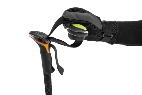 Une main portant un gant noir saisit la dragonne d'un bâton de ski noir.