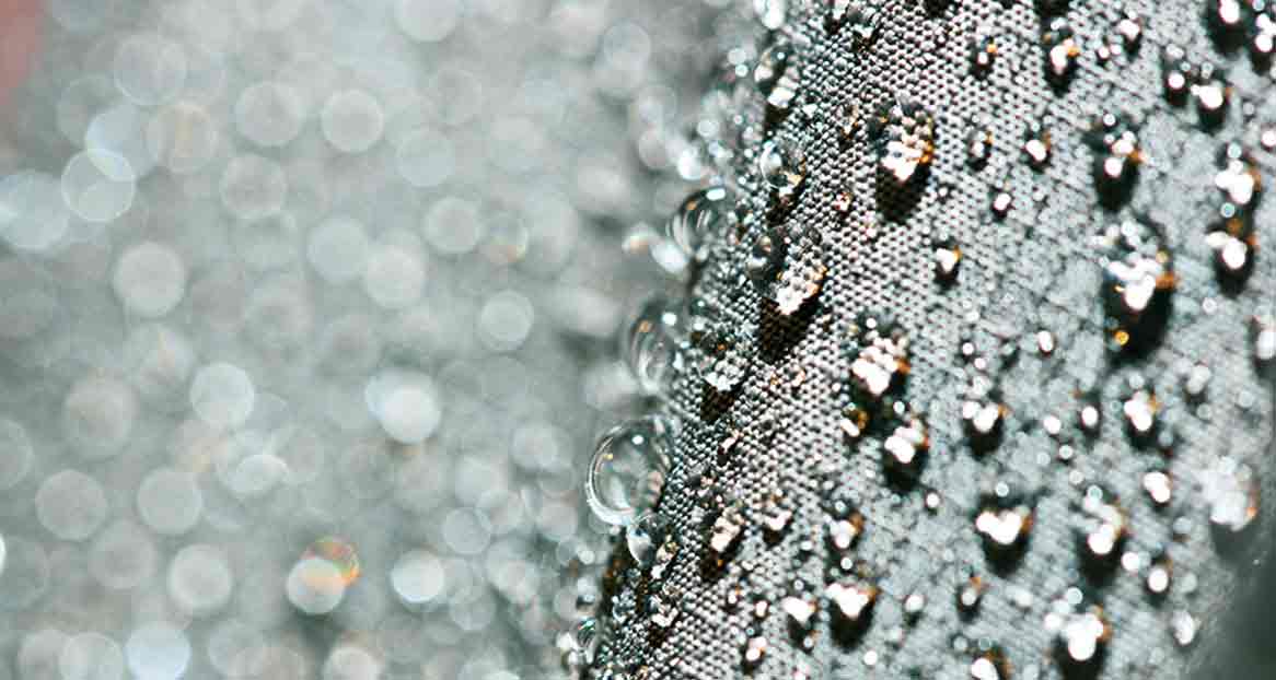 Drops of water on fabric Close-up of water droplets on a dark, textured fabric with blurred, circular lights in the background.