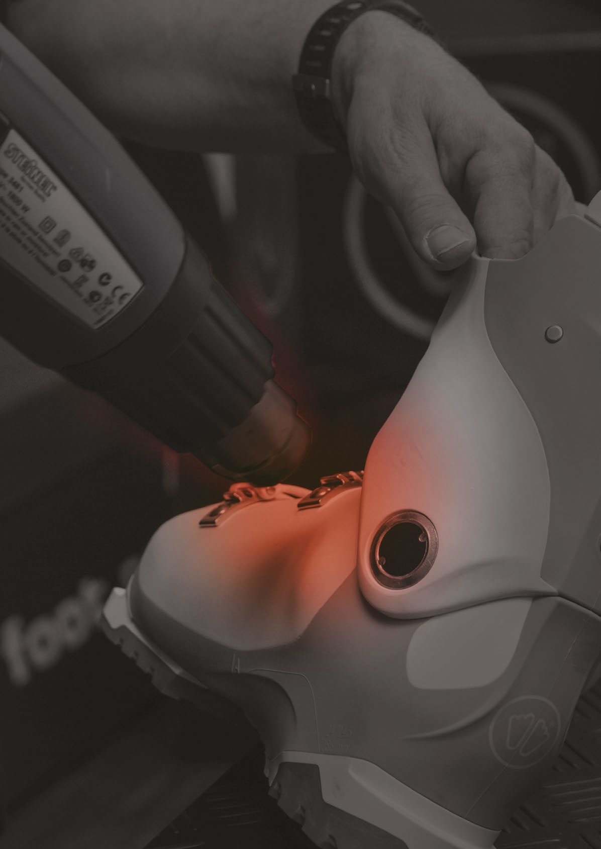 Une main tient un pistolet à air chaud qui irradie une chaussure de ski de chaleur orange pour l'ajuster.
