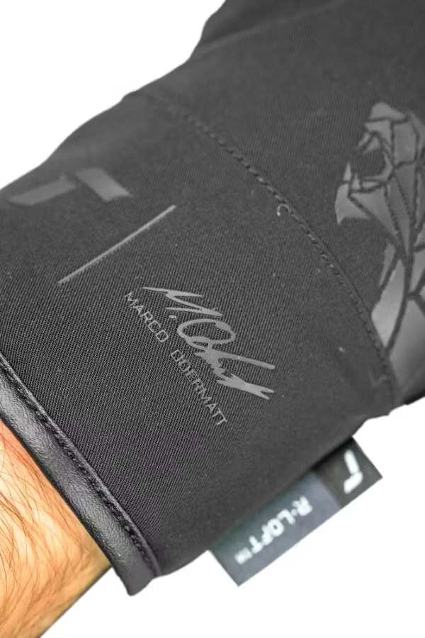 Detailaufnahme eines schwarzen Handschuhs mit Lederbündchen. Darauf ein Logo, der Schriftzug "Marco Odermatt" und ein Etikett mit "R-LOFT".
