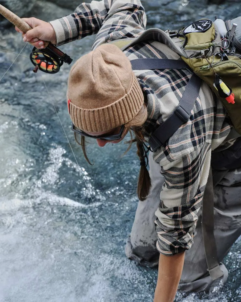 Person wearing a cashmere mix beanie while fishing in the water, wearing a plaid shirt and glasses.