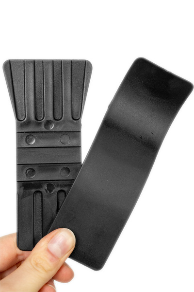 Eine Hand hält einen schwarzen, gerippten Kunststoffgegenstand neben einem glatten, gebogenen Kunststoffstreifen.