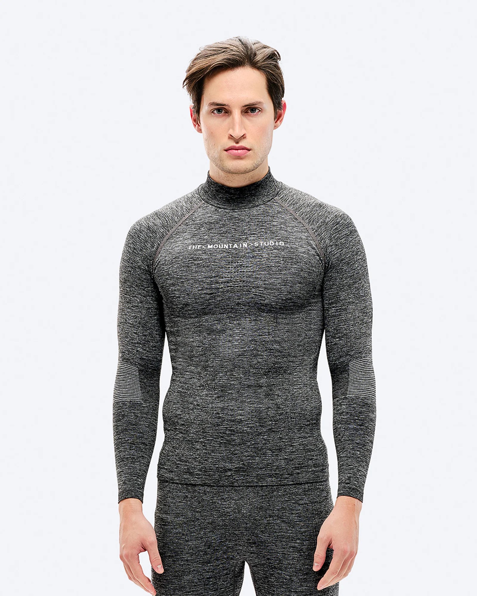 A man with brown hair wears gray sportswear with a long-sleeved top and pants against a white background.