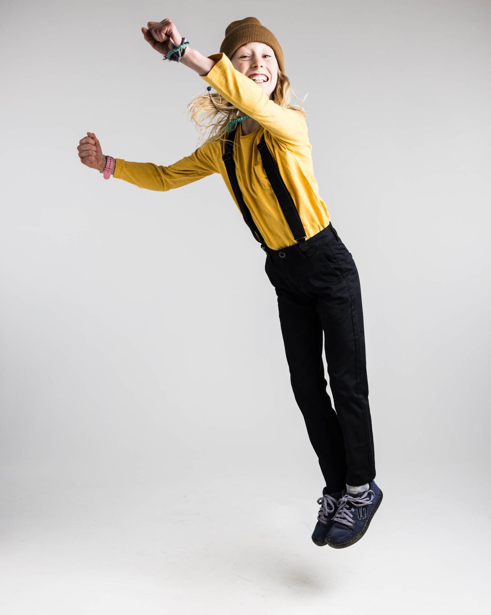 Une jeune fille au bonnet marron saute sur un fond blanc et tend les bras en l'air.