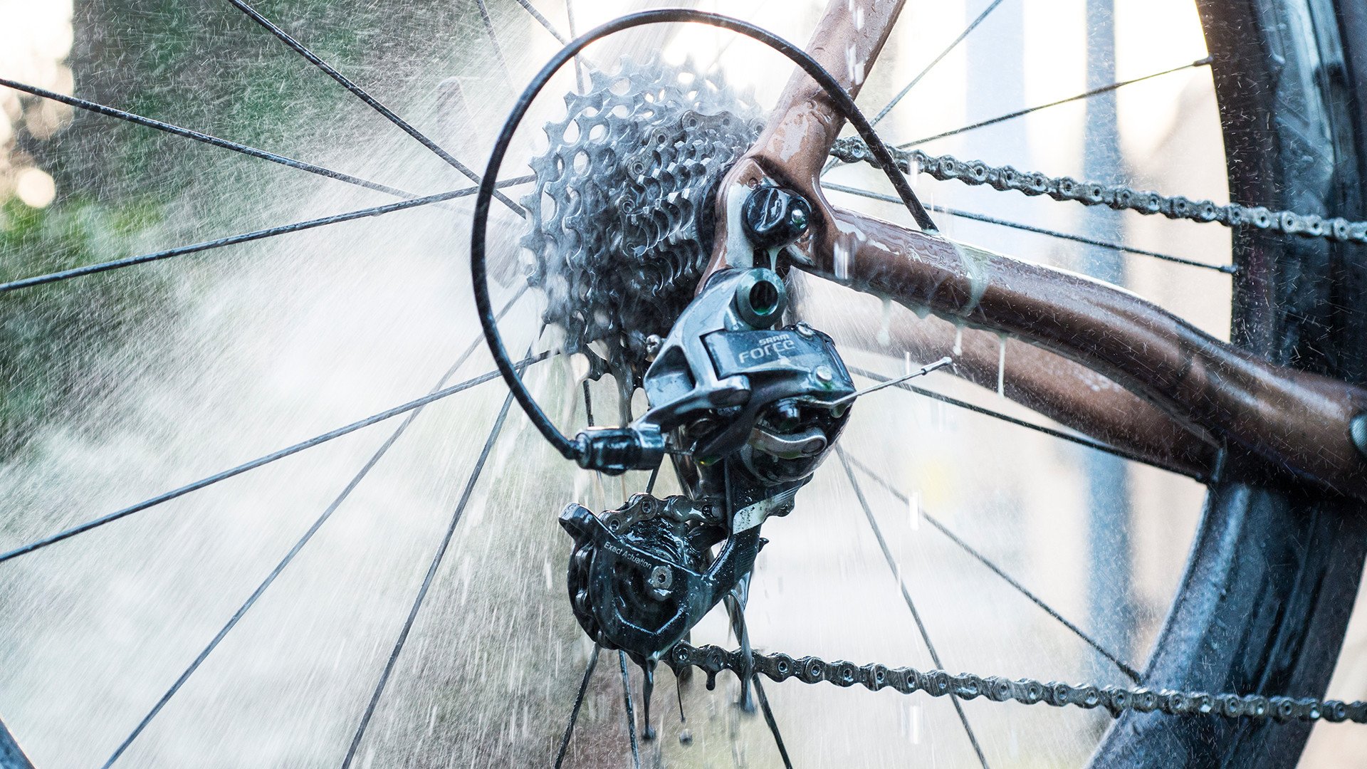 Nahaufnahme eines Fahrradantriebs unter Wasserstrahl. Kette, Kassette, Umwerfer sind sichtbar. Muc-Off Drivetrain Cleaner Anwendung.
