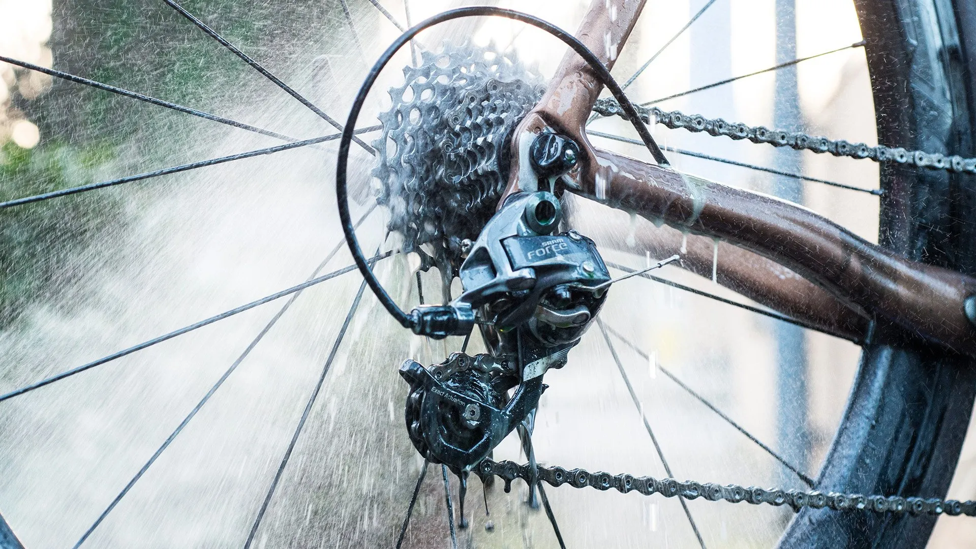 Nahaufnahme eines Fahrradantriebs unter Wasserstrahl. Kette, Kassette, Umwerfer sind sichtbar. Muc-Off Drivetrain Cleaner Anwendung.