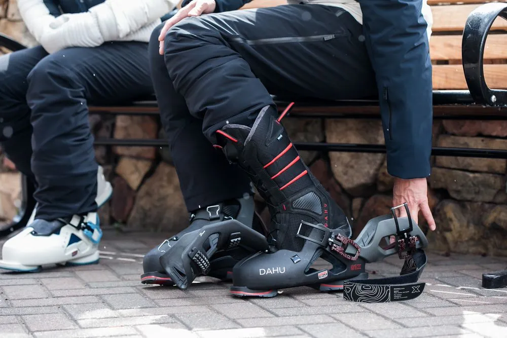 Deux personnes sont assises sur un banc. L'une d'elles porte des chaussures de ski DAHU et tient l'une d'entre elles dans sa main.