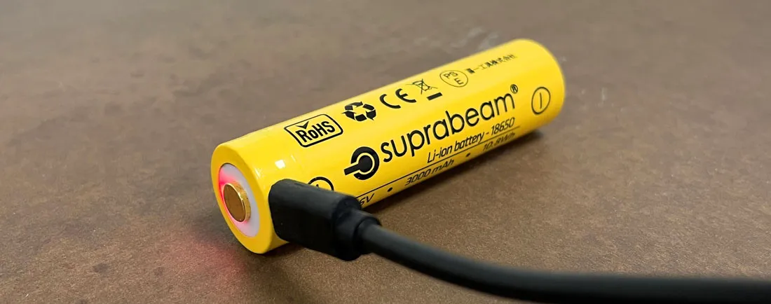 Yellow Suprabeam 18650 Li-Ion battery with USB cable for charging on brown surface.