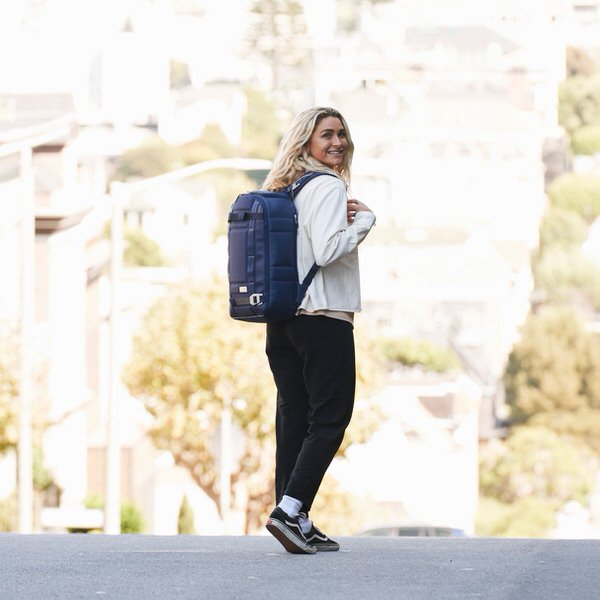 Person trägt einen dunkelblauen Rucksack auf der Straße. Der Douchebags The Backpack Deep Sea Blue Leather ist zu sehen.