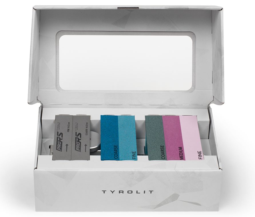 Offene, weiße Box mit Schleifklötzen in Grau-, Blau- und Pinktönen, beschriftet mit Fein, Mittel und Grob, Marke Tyrolit.