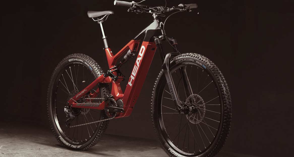 Un VTT électrique rouge et noir de la marque Head se tient devant un fond sombre qui reflète la lumière.