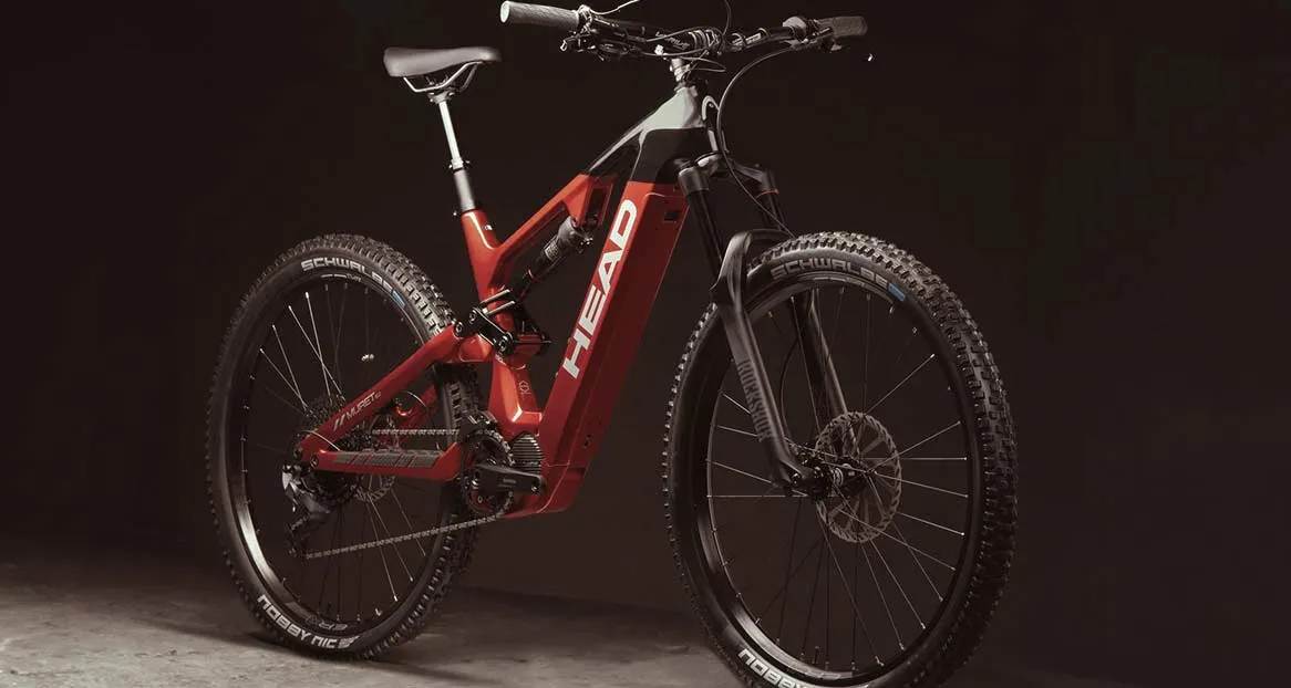 Ein rotes und schwarzes E-Mountainbike der Marke Head steht vor einem dunklen Hintergrund, das Licht reflektiert.
