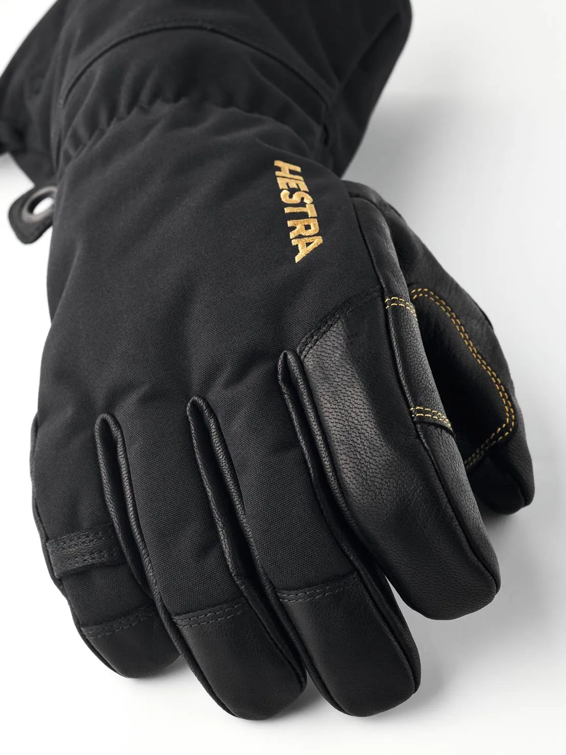 Close-up of a black Hestra Gore-Tex five-finger glove with leather details and gold Hestra lettering.