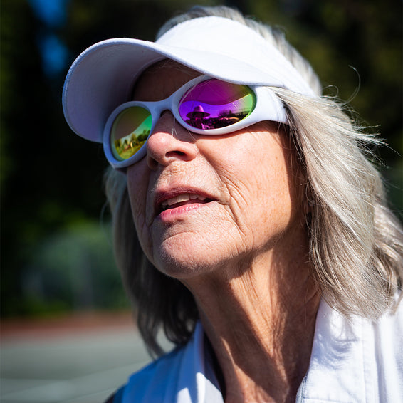 Ältere Frau mit grauem Haar und weißem Visor, trägt farbige The Slammer Miami Nights Sonnenbrille.