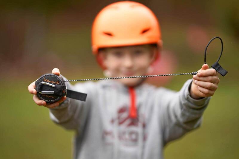 Un enfant portant un casque orange tient un système de traction noir dans ses mains et le présente à la caméra.