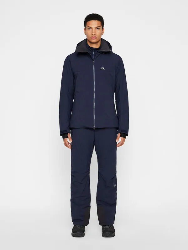 Un uomo indossa pantaloni da sci J.Lindeberg Truulli di colore navy e una giacca abbinata.