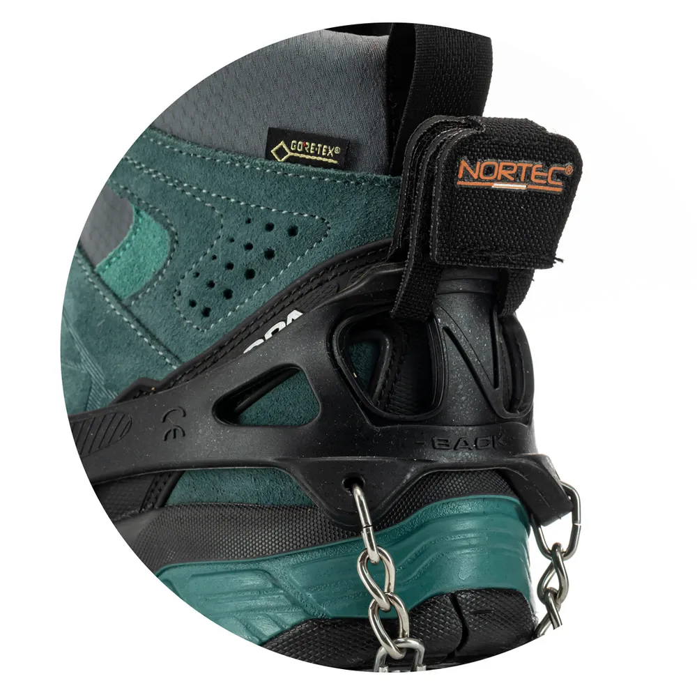 Detailaufnahme: Trekking-Steigeisen an Bergschuh befestigt. Schwarzes Elastomer mit Kette und Stahlplatten an grün-grauem Schuh.