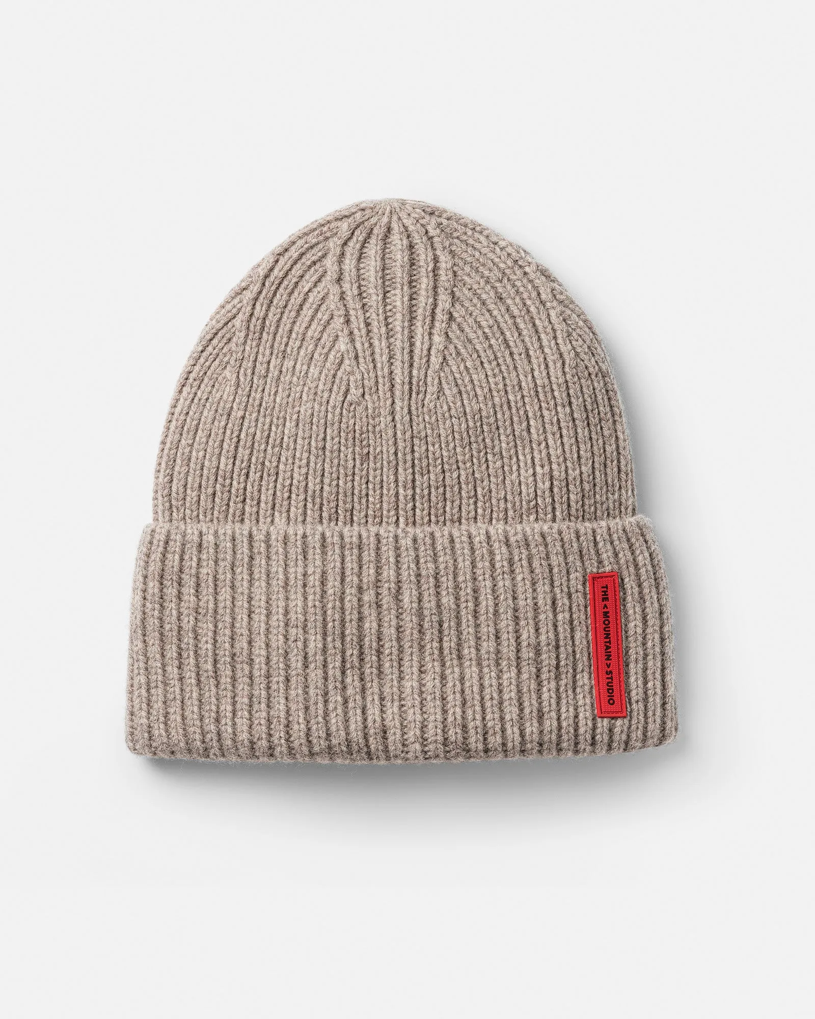 Cappello di lana a coste di colore beige con etichetta rossa su superficie bianca.
