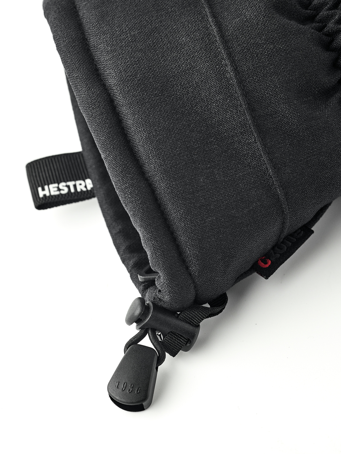 Black Hestra mittens Close-up of a black Hestra mitten with drawstring and "1936" on the stopper. A band with the inscription "Hestra" is visible.