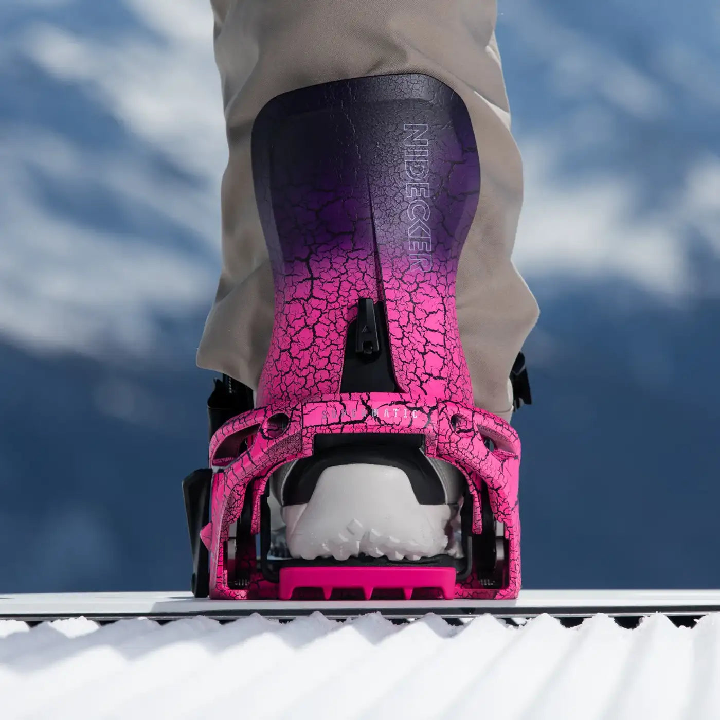 Defekte Snowboardbindung Nahaufnahme einer pinkfarbenen Snowboardbindung mit Rissen auf einem Snowboard vor verschwommenem, blauem Hintergrund.