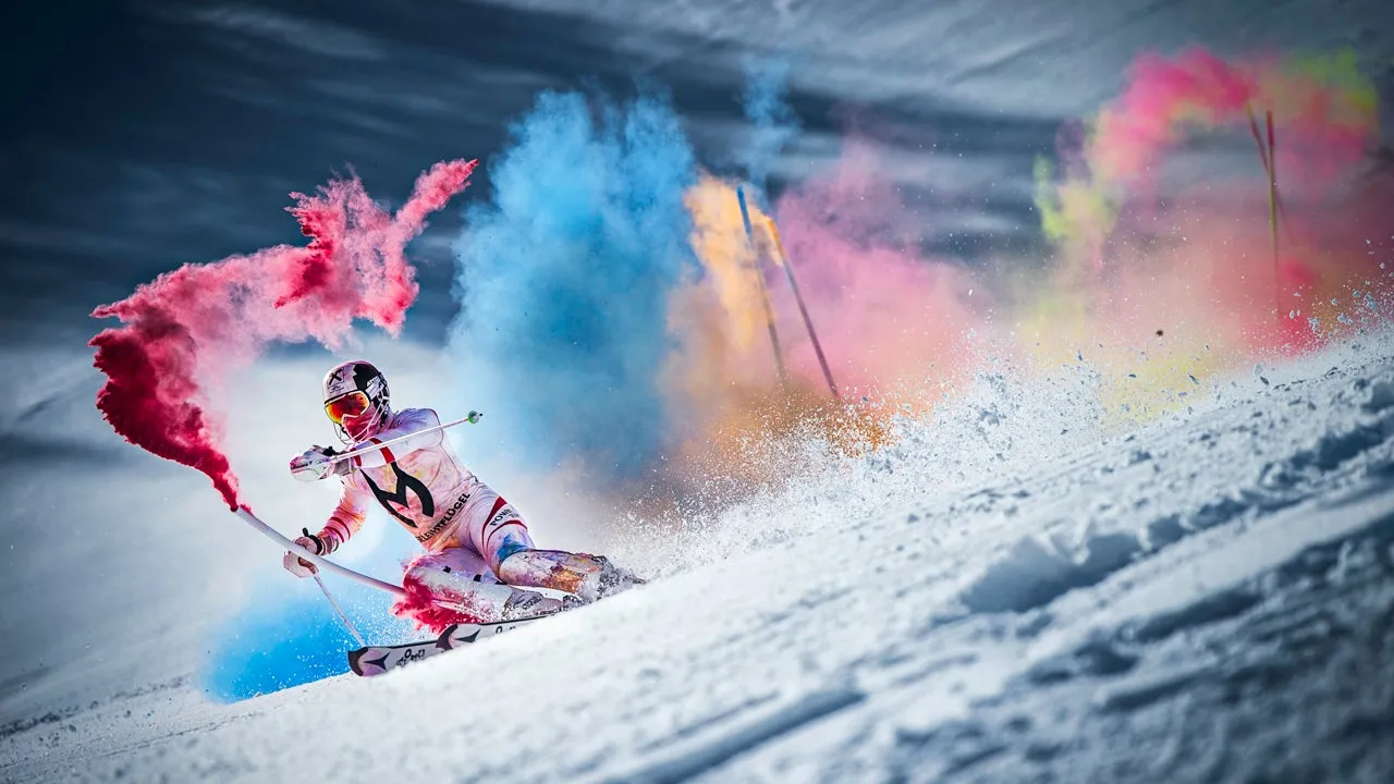 Uno sciatore sta scendendo lungo un pendio innevato, circondato da fumo colorato rosso, blu, giallo e rosa.