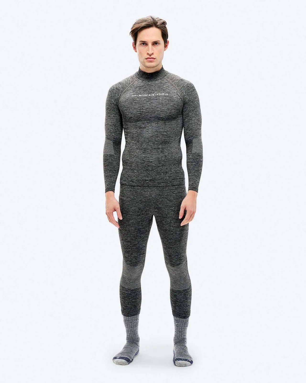 Ein Mann in grauer Sportunterwäsche und Socken steht vor einem weißen Hintergrund.