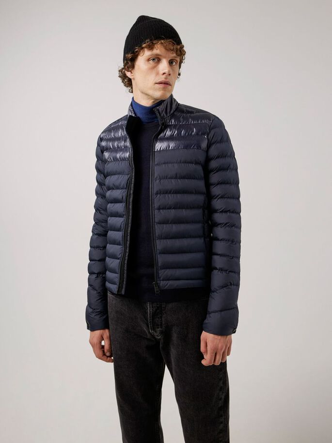 Ein Mann mit Mütze trägt eine dunkelblaue, gesteppte Rick Light Jacket über einem Rollkragenpullover.