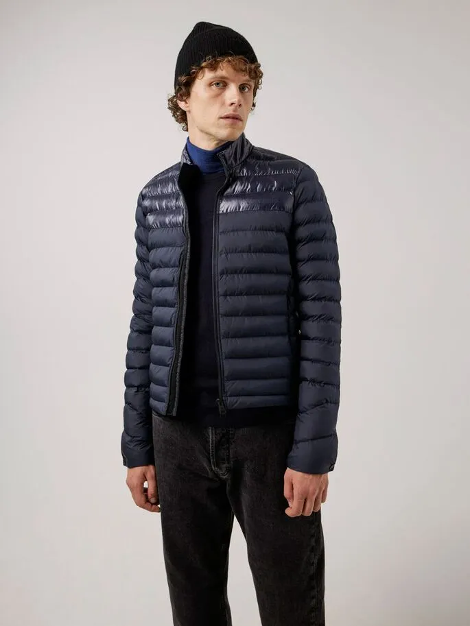 Un uomo con un berretto indossa una giacca trapuntata Rick Light blu scuro su un maglione a collo alto.