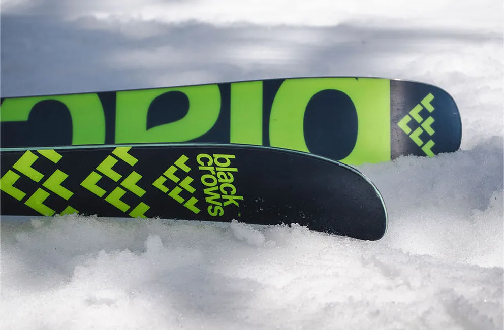 Close-up of Black Crows Atris ski ends in the snow. Green logo on black background.