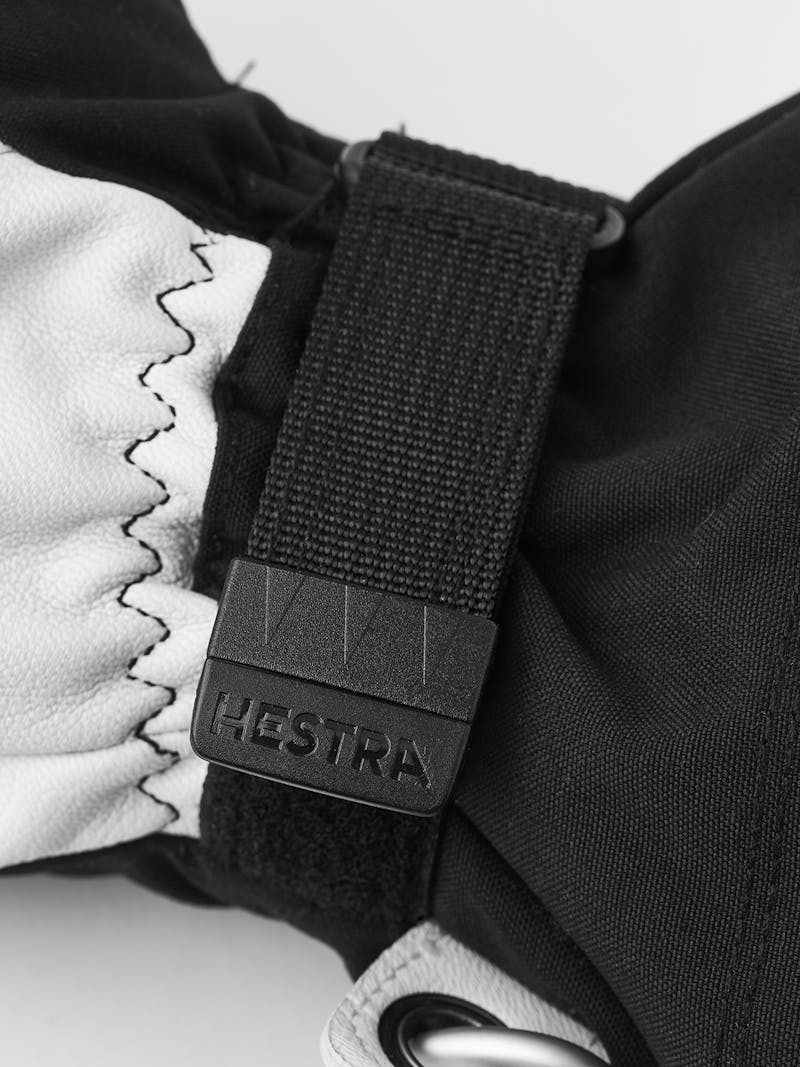 Detailansicht des Hestra Army Leather Heli Ski Mitt, zeigt Leder, Stoff und den Markennamen auf dem Verschluss.