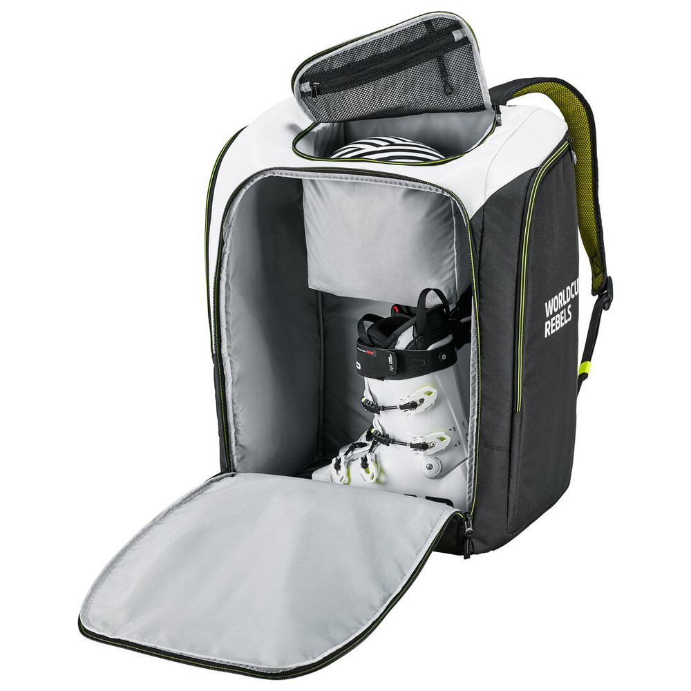 Opened, large, white-black-green Rebels Racing backpack. Ski boot is visible in the main compartment, helmet in helmet pocket.