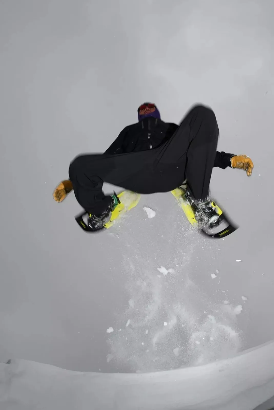 A man jumps over a snow-covered surface on yellow Tubbs VRT 29 snowshoes.