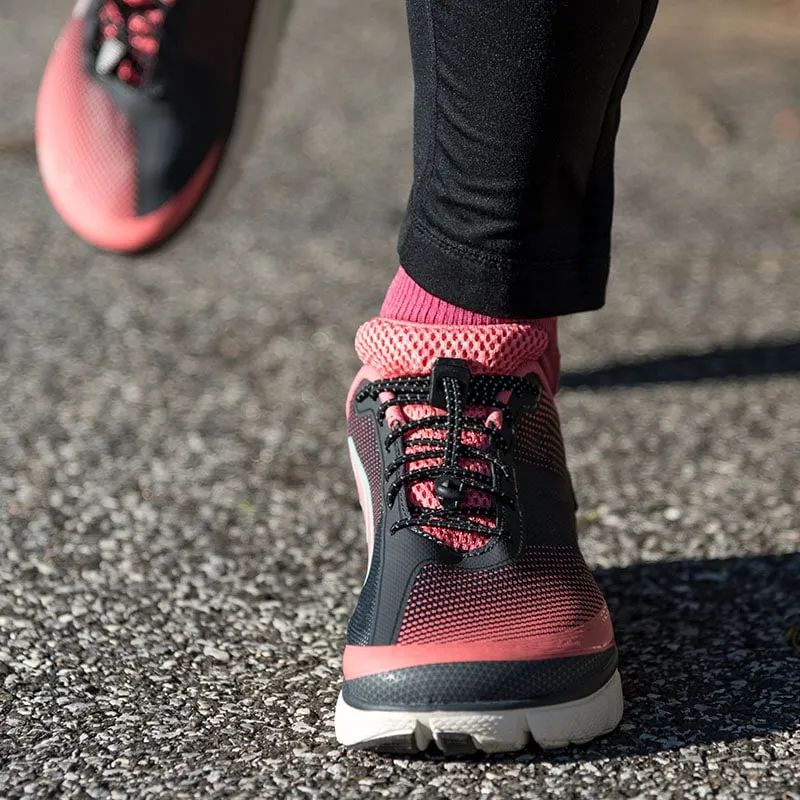 Close-up of running shoes with black elastic laces and pink socks on asphalt.