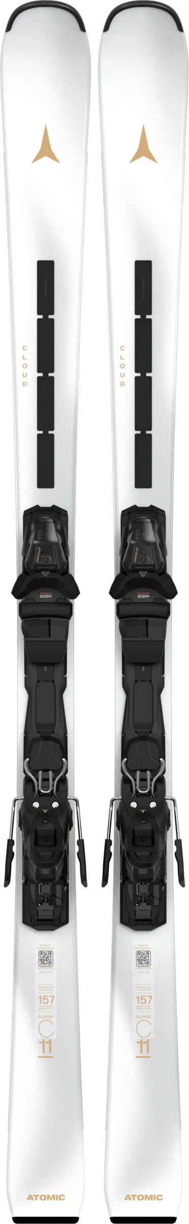 Two white skis with black bindings are standing vertically next to each other. Golden markings and lettering can be seen on the skis.