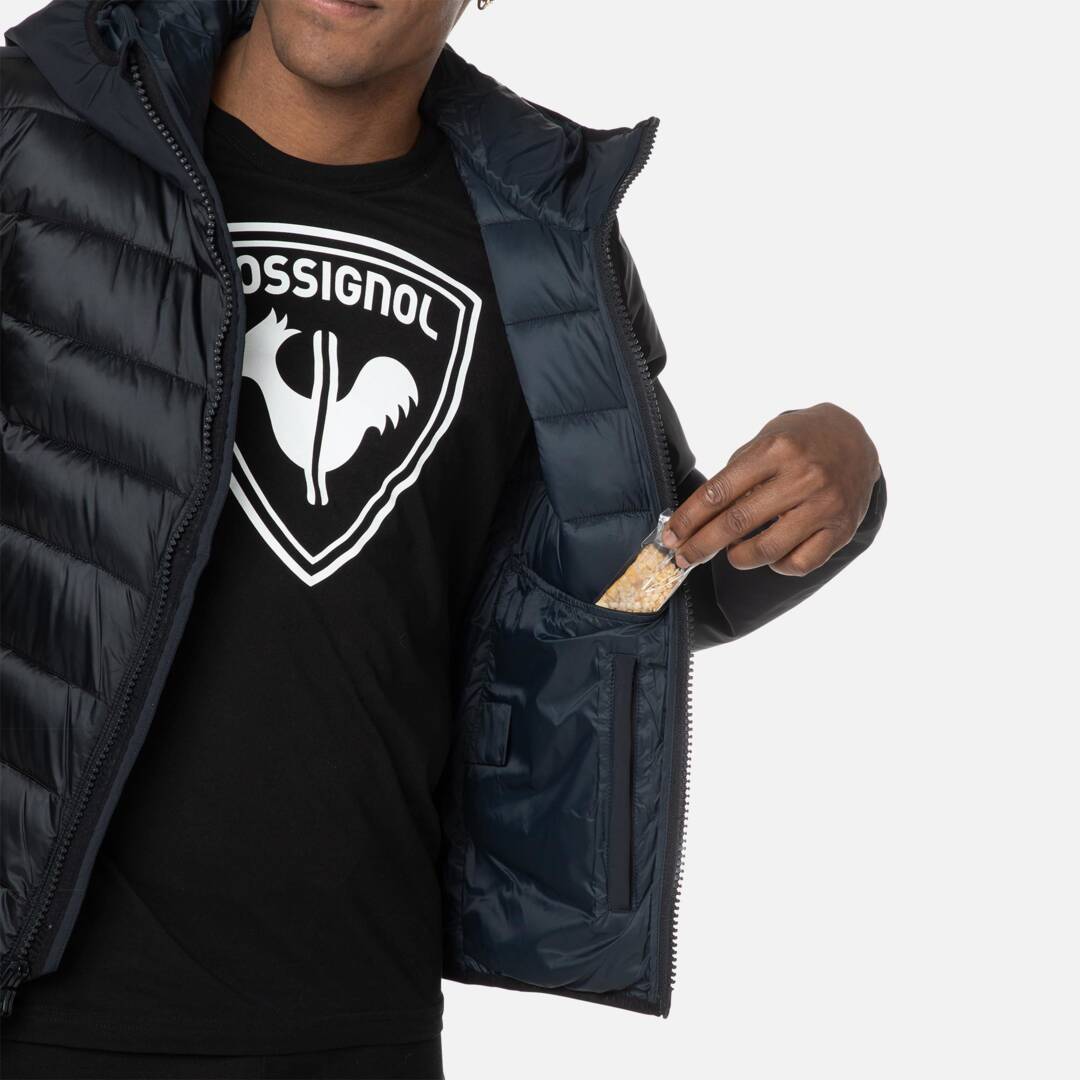 Dunkelblauer Rossignol Hoodie Geöffnete, gesteppte, dunkelblaue Rossignol Hoodie Jacke; Mann nimmt Riegel aus Innentasche.