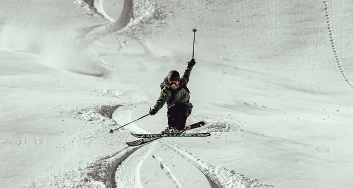 Ein Skifahrer fährt in steilem Gelände mit einer Hand mit einem Stock hoch in der Luft.