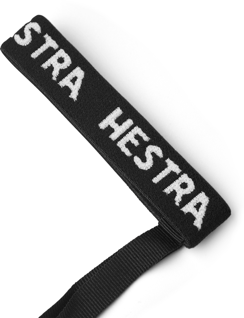 Bande textile noire avec inscription blanche "STRA HESTRA" et bande noire à une extrémité, sur fond blanc.
