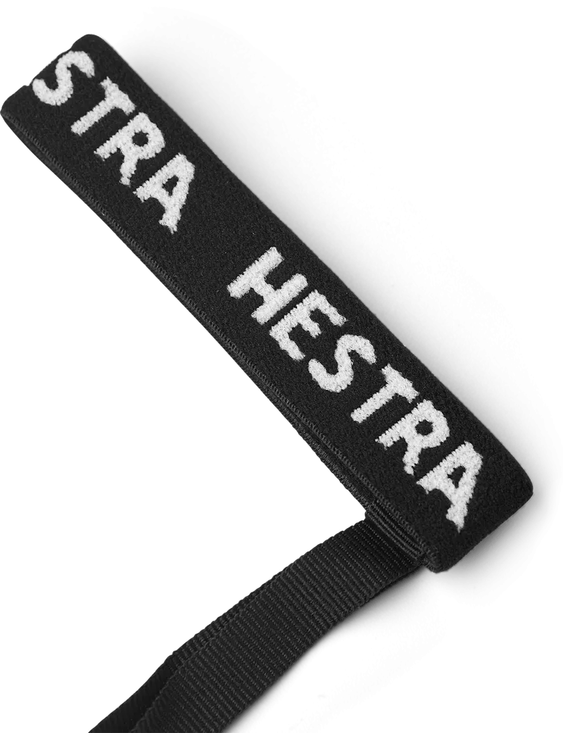 Schwarzes Textilband mit weißem "STRA HESTRA" Schriftzug und schwarzem Band an einem Ende, auf weißem Grund.