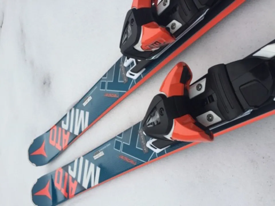 Due Atomic Ski blu con accenti arancioni giacciono su neve chiara, gli attacchi sono neri e arancioni.