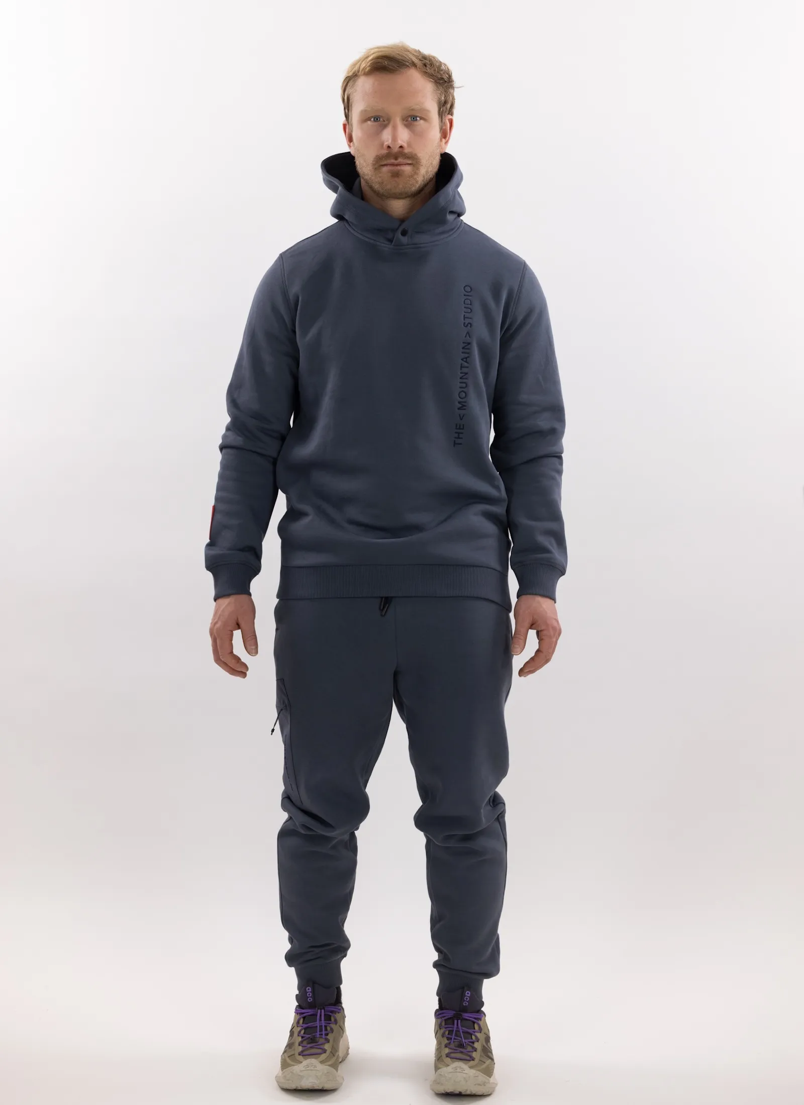Man in gray Z-5 3L Hybrid Shell Jacket and matching pants from The Mountain Studio against a white background.