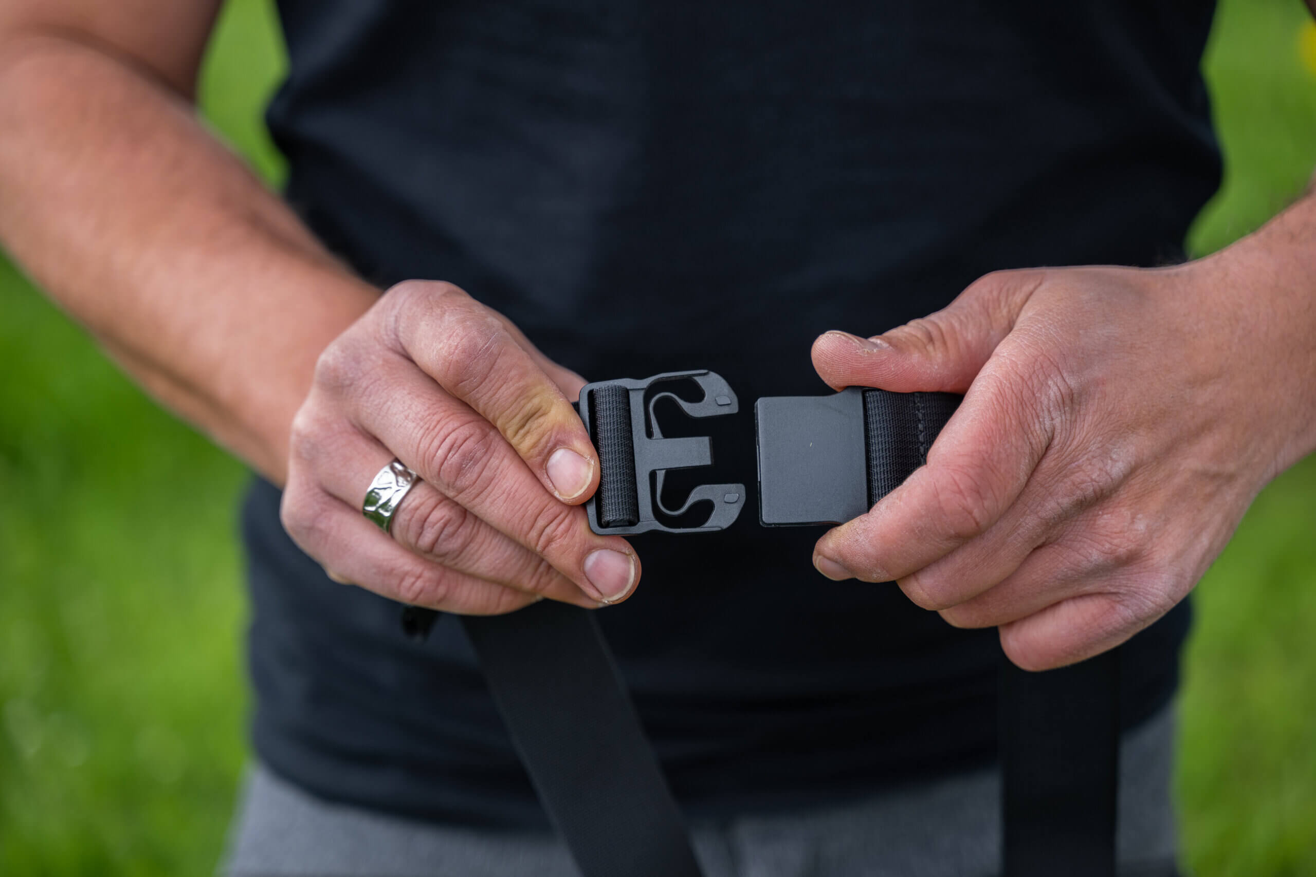 Person öffnet schwarzen Outdoor-Gürtel mit Schnalle. Hände mit Ring sind sichtbar.