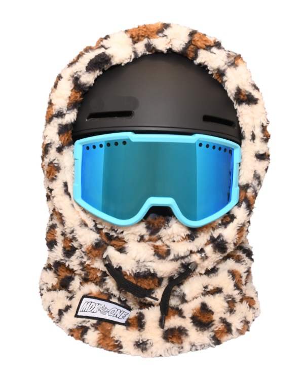 Cagoule enfant en peluche moelleuse, tons marron chauds à motif Jaguar, sur casque de ski noir. Lunettes de ski bleu clair à verres miroirs par-dessus. La peluche recouvre tête, cou et visage ; cordons noirs devant.