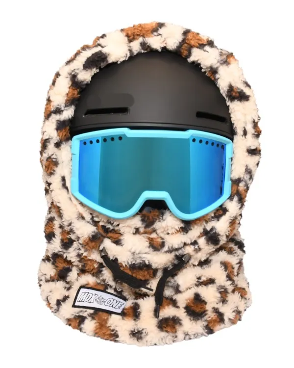 Fluffy children's balaclava in warm brown tones with a Jaguar pattern, worn over a black ski helmet. Bright light blue ski goggles with mirrored lenses sit on top. Soft plush covers the head, neck, and face; black drawstrings at the bottom.