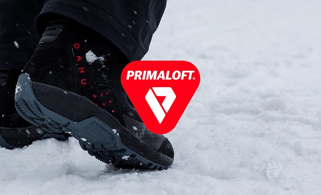 Chaussure de ski noire Dahu Gros plan sur une chaussure de ski noire Dahu avec le logo Primaloft rouge dans la neige.