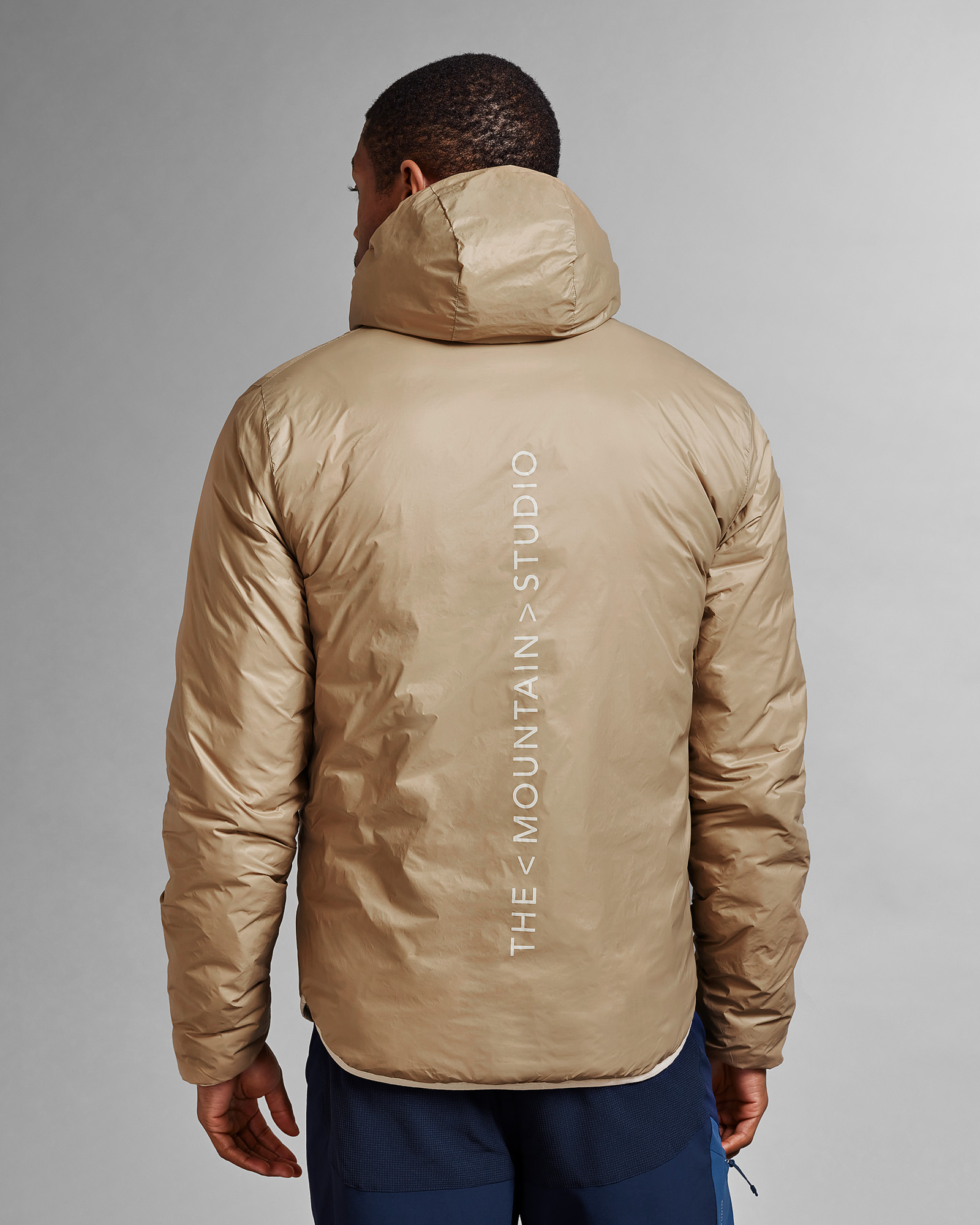 Beige Wendejacke Rückansicht einer beigen D-3L Reversible Light Hood Jacket mit Kapuze, bedruckt mit "THESTUDIO".