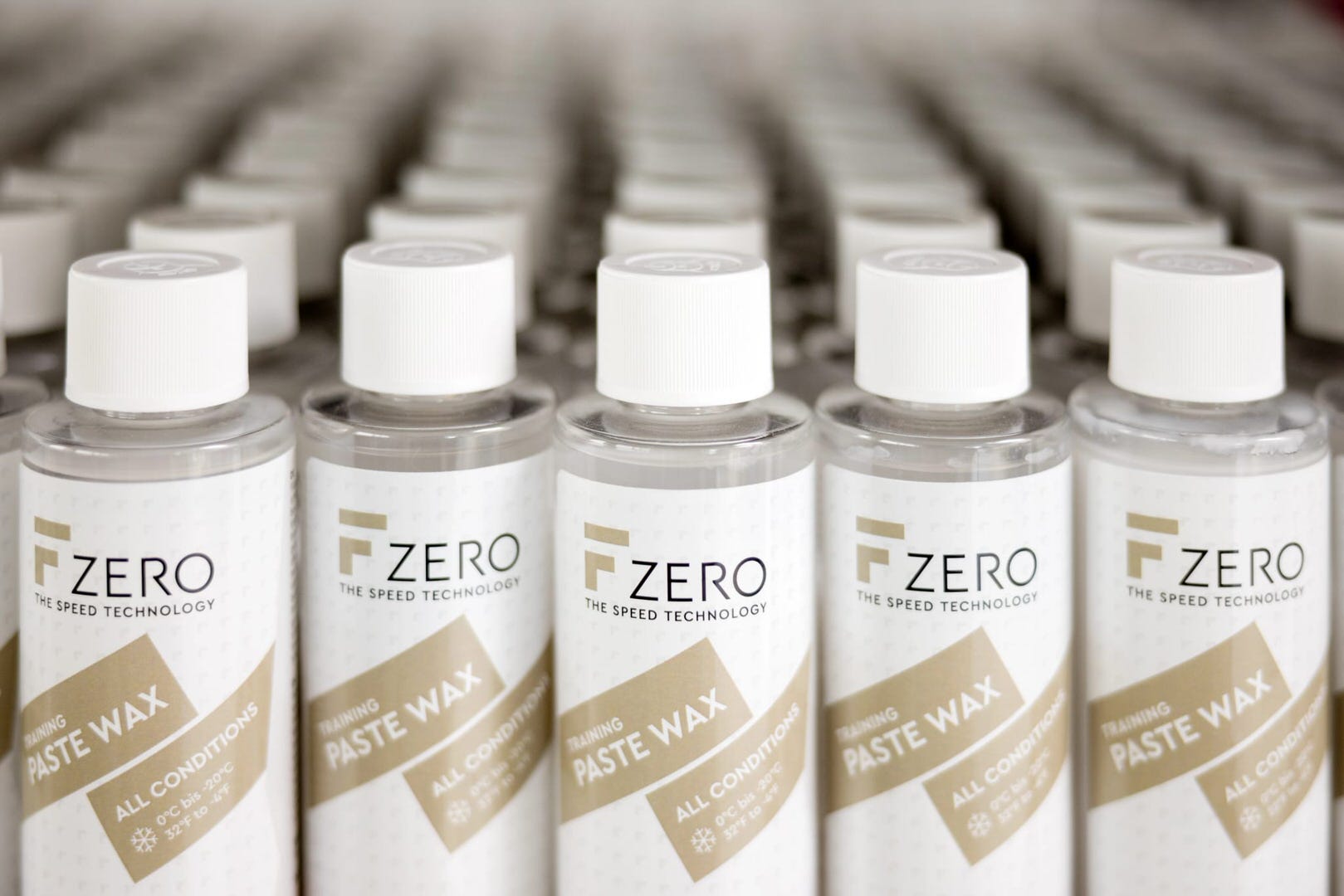 De nombreuses bouteilles de F Zero Paste Wax avec des bouchons blancs sur plusieurs rangées. Sur les étiquettes, on peut lire le logo et "Paste Wax".