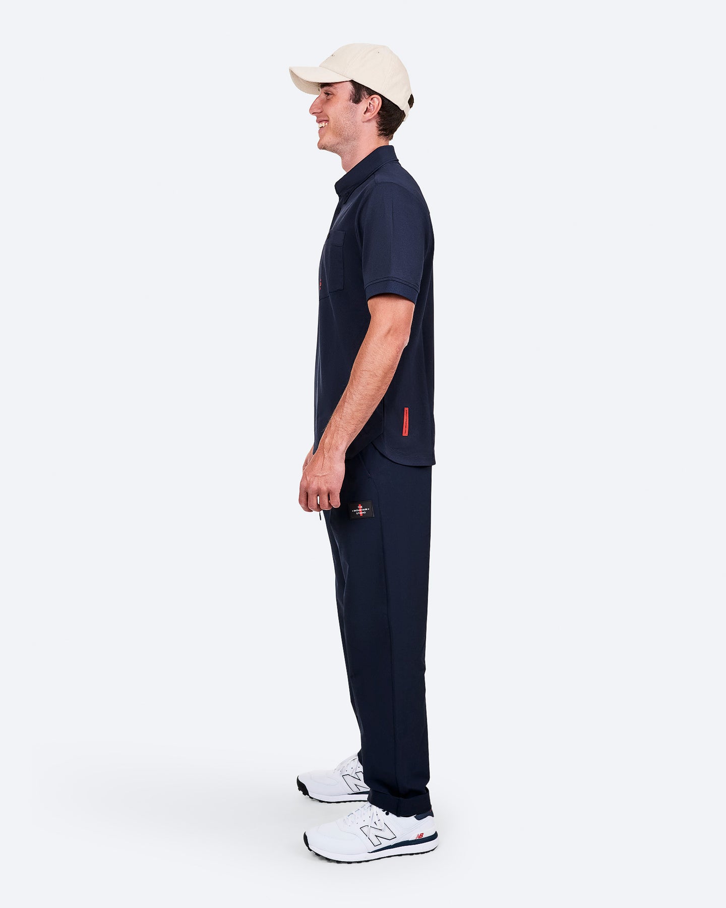 Homme de côté, en polo bleu marine, pantalon de jogging et baskets blanches, avec casquette beige.