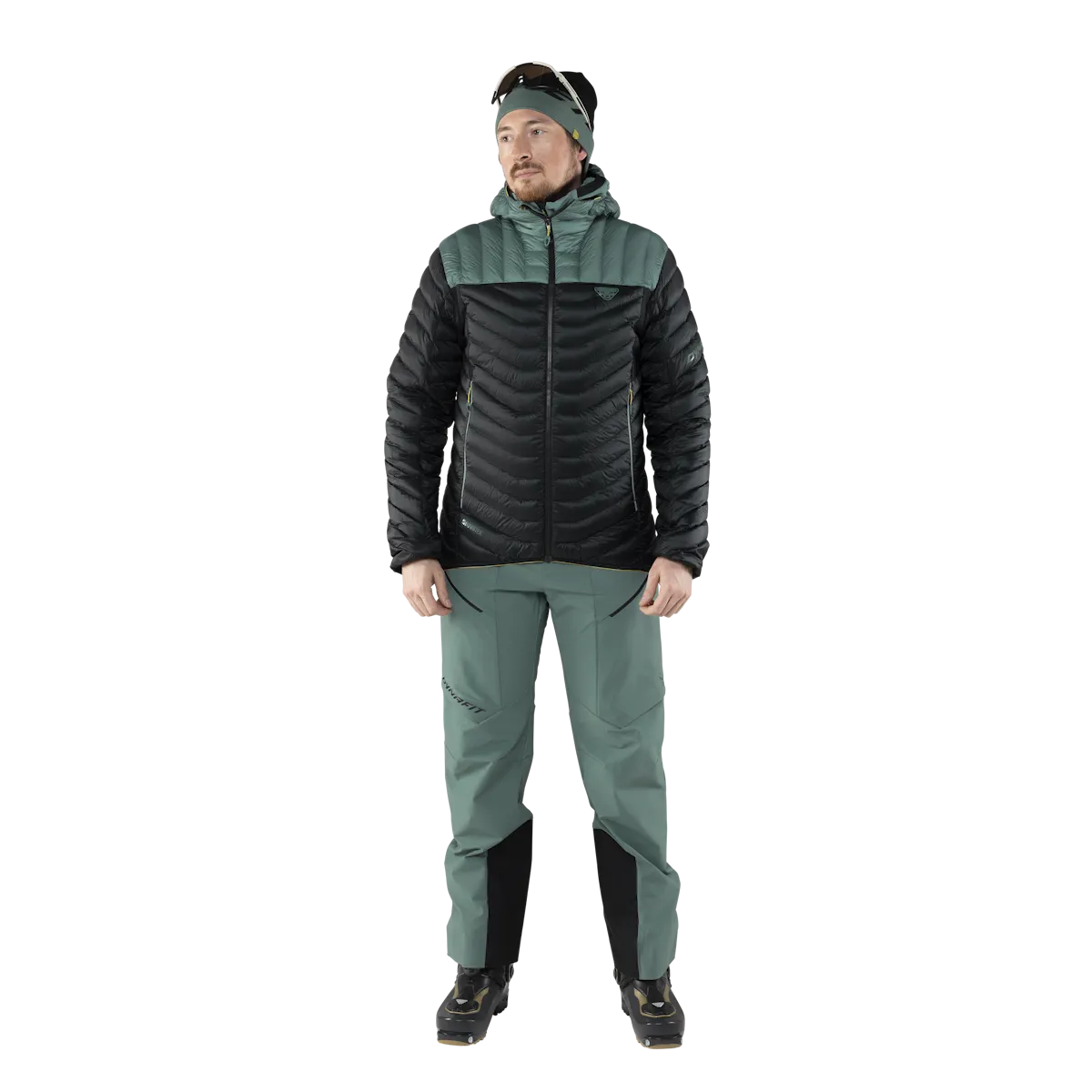 Uomo in piumino e pantaloni da sci alpinismo, su sfondo bianco. La giacca è nera e verde.