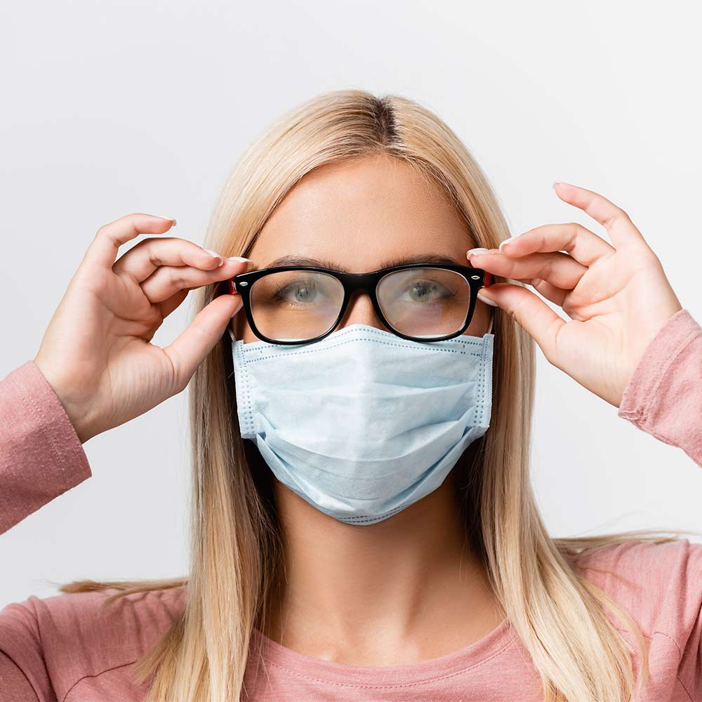 Femme portant un masque dont les lunettes sont embuées. Focus sur les verres de lunettes embués. Fog-Out anti-buée microfibre.
